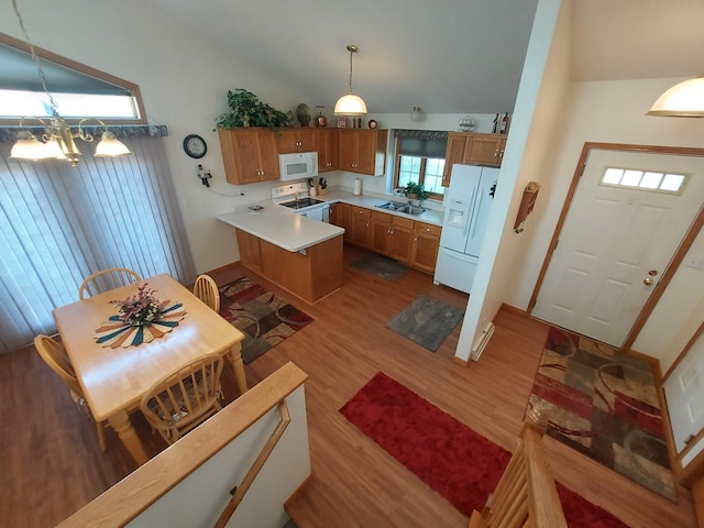 kitchen featuring white appliances, a sink, wood finished floors, brown cabinetry, and lofted ceiling