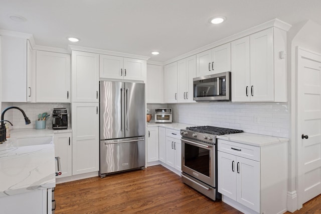 kitchen featuring high quality appliances, a sink, backsplash, white cabinets, and light stone countertops