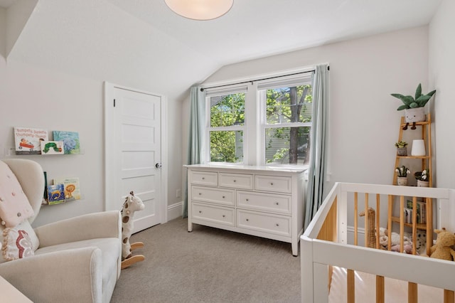 bedroom with lofted ceiling, a crib, and light carpet