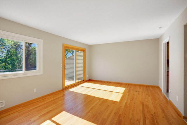 empty room with healthy amount of natural light, light wood-style flooring, and baseboards