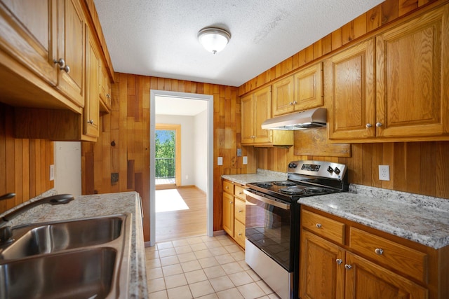 kitchen featuring electric stove, under cabinet range hood, a sink, wood walls, and light tile patterned floors