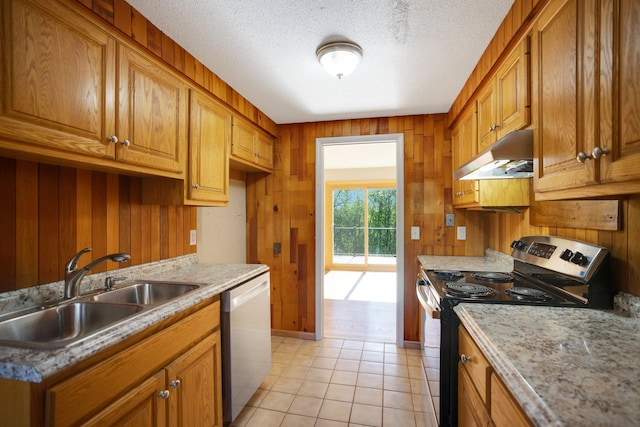 kitchen featuring appliances with stainless steel finishes, under cabinet range hood, a sink, brown cabinets, and wooden walls