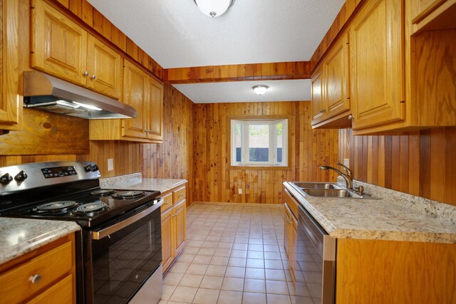 kitchen featuring stainless steel appliances, under cabinet range hood, a sink, wooden walls, and light countertops