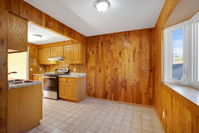 kitchen featuring electric stove, under cabinet range hood, a sink, wood walls, and light tile patterned floors