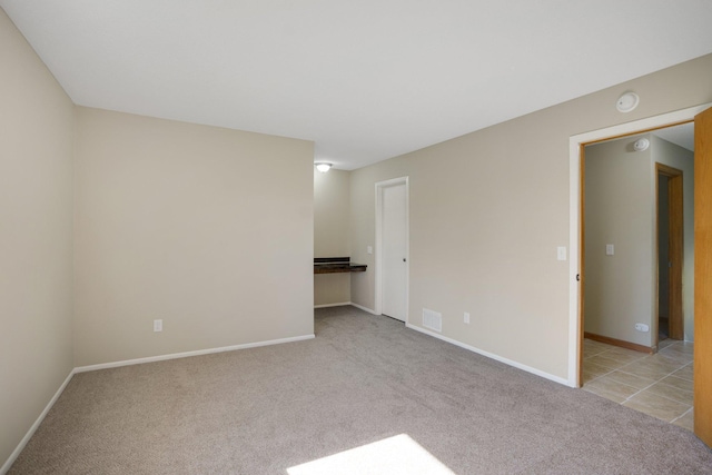 spare room featuring light colored carpet, baseboards, and a smoke detector