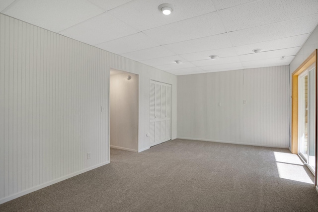 carpeted spare room featuring a paneled ceiling and baseboards