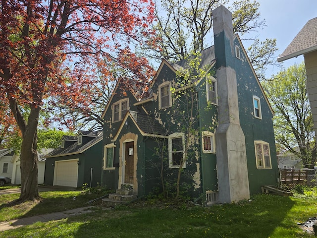 english style home with an attached garage, a chimney, and stucco siding