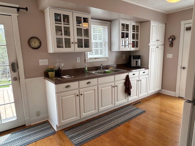 12176 2nd St, Northome, MN 56661 - kitchen with dark countertops, white cabinets, light wood-type flooring, glass insert cabinets, and a wainscoted wall