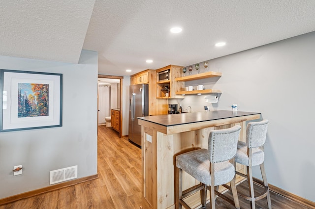 49935 Acacia Trl, Nessel Twp, MN 55080 - kitchen with stainless steel fridge, a kitchen bar, light wood finished floors, a textured ceiling, and open shelves