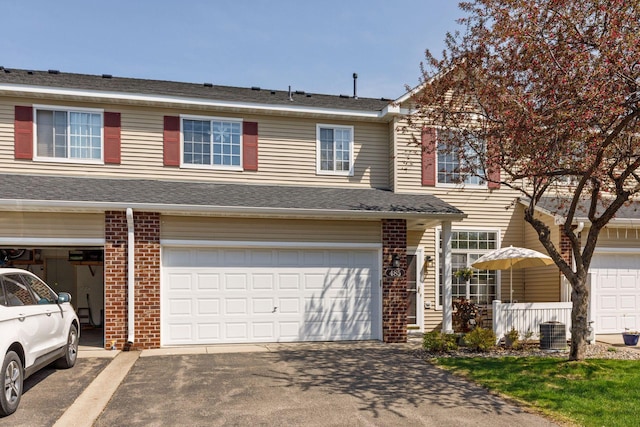 view of property featuring asphalt driveway, an attached garage, cooling unit, and brick siding