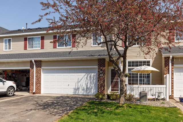 view of property with brick siding, an attached garage, cooling unit, asphalt driveway, and a shingled roof