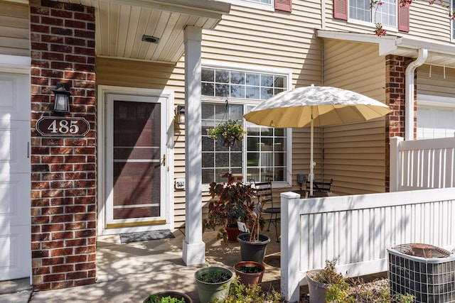 property entrance with central AC unit, brick siding, and fence