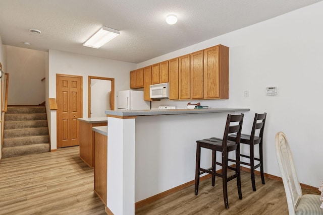 kitchen with white appliances, light wood finished floors, a peninsula, a breakfast bar area, and a textured ceiling