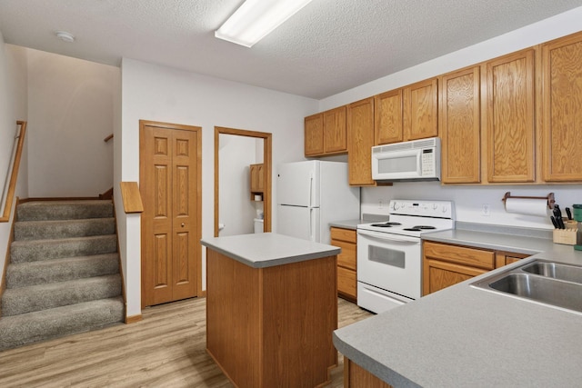 kitchen featuring white appliances, a sink, a center island, light wood-style flooring, and a textured ceiling