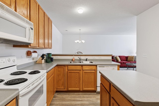 kitchen featuring white appliances, a sink, a peninsula, light wood-style floors, and a chandelier