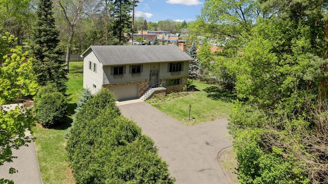 bi-level home with asphalt driveway, stone siding, a chimney, a front lawn, and an attached garage