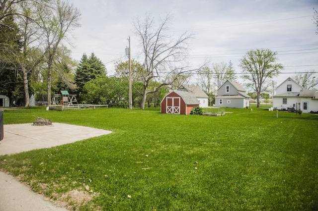 view of green lawn featuring a storage shed, an outdoor fire pit, an outdoor structure, a playground, and a patio area