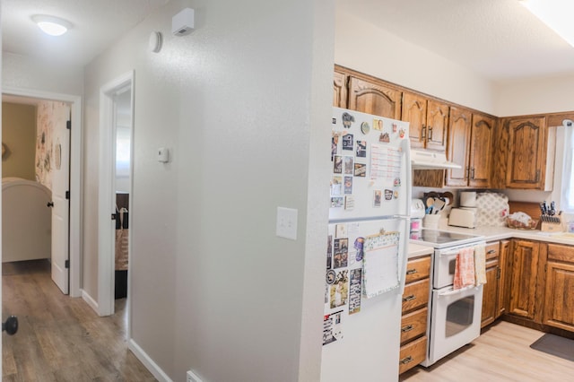 kitchen featuring white appliances, under cabinet range hood, light wood-style flooring, brown cabinetry, and light countertops