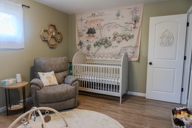 bedroom with a nursery area, wood finished floors, and baseboards