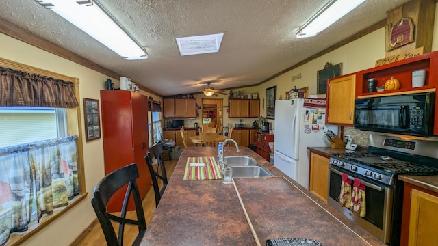 kitchen featuring black microwave, stainless steel gas range, a sink, dark countertops, and freestanding refrigerator