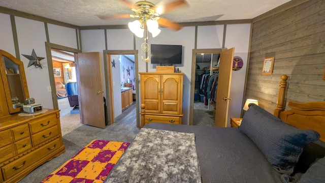 bedroom featuring carpet flooring, wood walls, a walk in closet, a closet, and ceiling fan