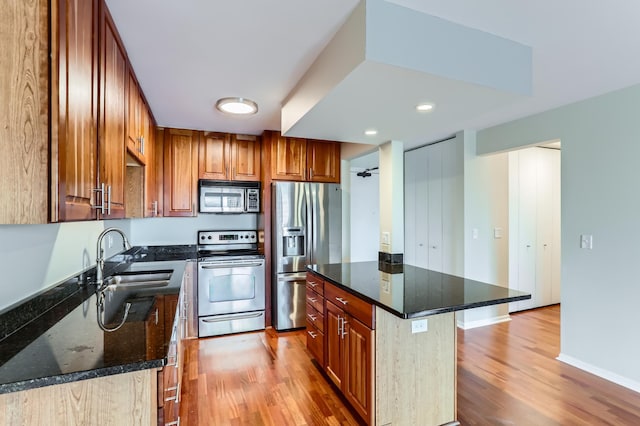 kitchen featuring appliances with stainless steel finishes, light wood-style floors, a sink, dark stone countertops, and brown cabinetry