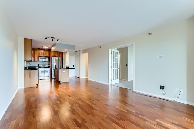 unfurnished living room featuring light wood-style flooring, track lighting, baseboards, and a sink