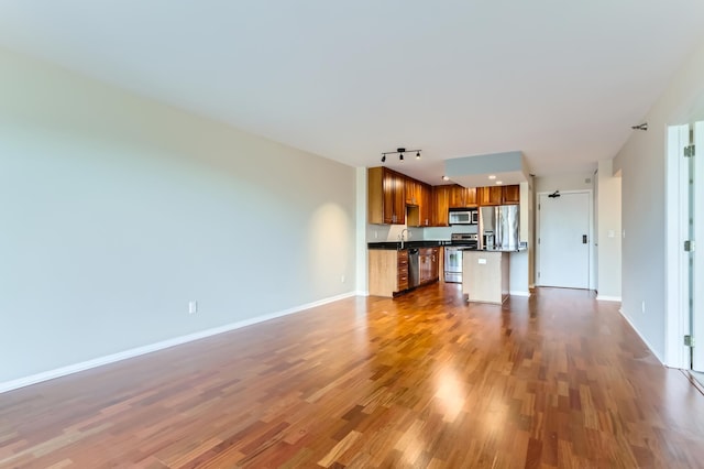unfurnished living room featuring dark wood-type flooring, baseboards, track lighting, and a sink