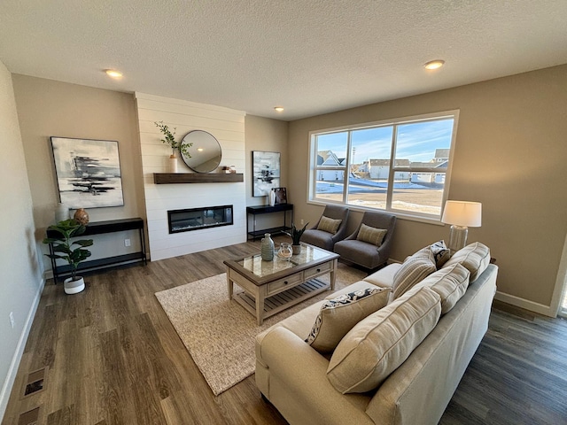 living room featuring wood finished floors, baseboards, a large fireplace, a textured ceiling, and recessed lighting