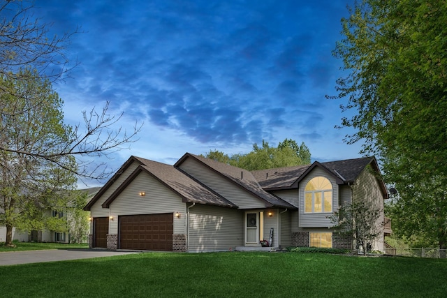 split level home with a garage, a front lawn, concrete driveway, brick siding, and a shingled roof