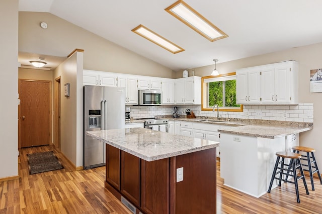 kitchen featuring appliances with stainless steel finishes, lofted ceiling, light wood-type flooring, a peninsula, and white cabinetry