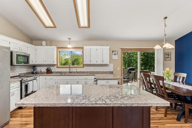 kitchen featuring appliances with stainless steel finishes, a sink, tasteful backsplash, light wood-style flooring, and vaulted ceiling