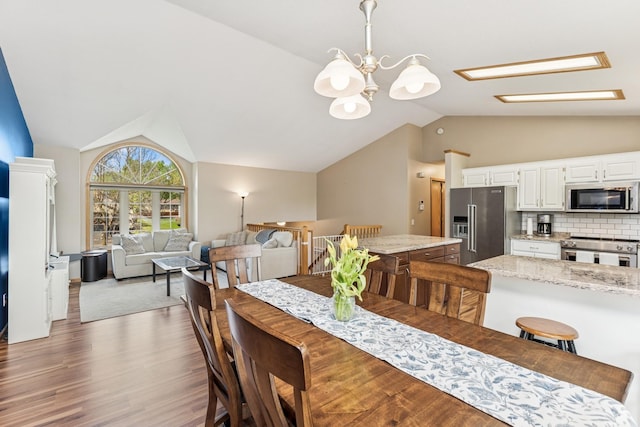 dining space with lofted ceiling, wood finished floors, a skylight, and a chandelier