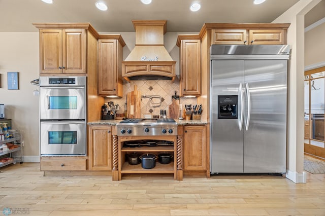 3914 21st Ave S, Moorhead, MN 56560 - kitchen featuring appliances with stainless steel finishes, premium range hood, light stone countertops, light wood finished floors, and tasteful backsplash