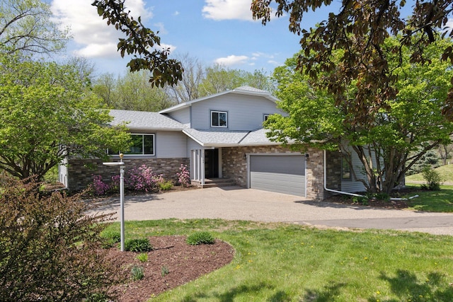 view of front of house with driveway, roof with shingles, stone siding, a front yard, and a garage