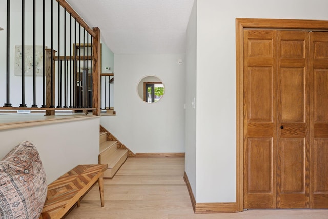 hallway featuring light wood-style floors, baseboards, and stairway