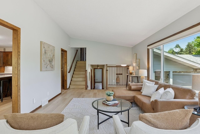 living room featuring vaulted ceiling, light wood-style flooring, stairs, and baseboards