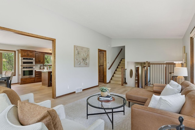 living area featuring light wood-style floors, stairway, and baseboards