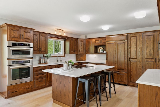 kitchen with black electric cooktop, light wood-style floors, double oven, and light countertops