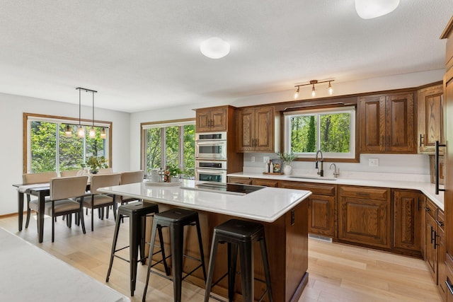 kitchen featuring a sink, black electric stovetop, stainless steel double oven, light countertops, and a breakfast bar