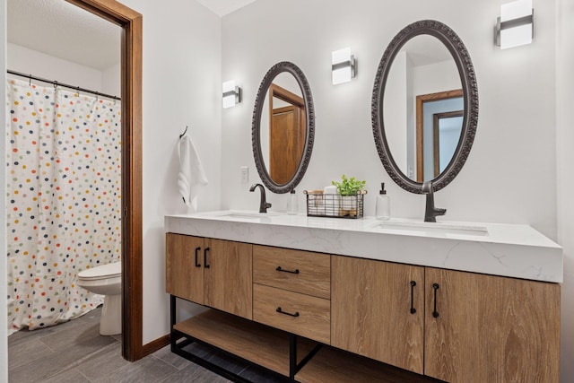full bath featuring toilet, double vanity, and baseboards