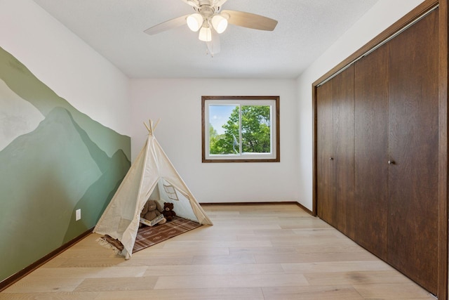 game room featuring light wood-style flooring, a ceiling fan, and baseboards