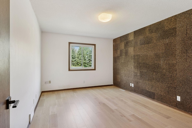 spare room with light wood-style flooring, an accent wall, and baseboards