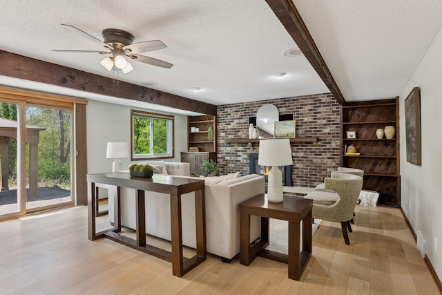 living room featuring a textured ceiling, light wood-style flooring, ceiling fan, a brick fireplace, and built in shelves