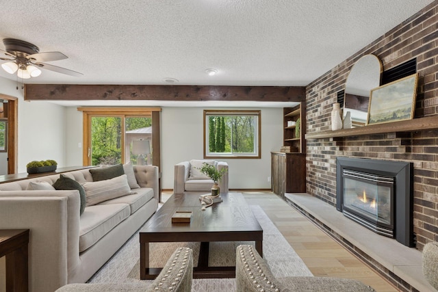 living area with a textured ceiling, light wood-style floors, a brick fireplace, and ceiling fan