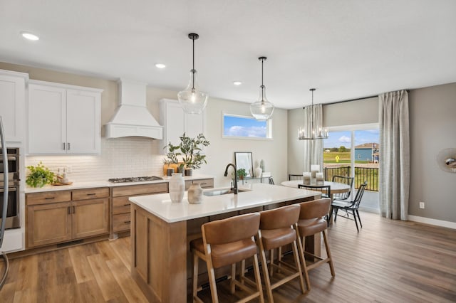 kitchen featuring a sink, custom range hood, gas cooktop, an island with sink, and light wood-style flooring