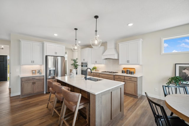 kitchen with appliances with stainless steel finishes, a sink, custom exhaust hood, backsplash, and wood finished floors