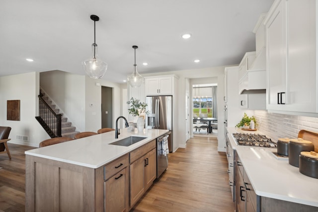 kitchen featuring a sink, appliances with stainless steel finishes, backsplash, light wood finished floors, and a kitchen island with sink