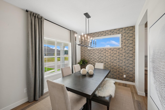 dining area featuring a chandelier, light wood-style flooring, wallpapered walls, and baseboards