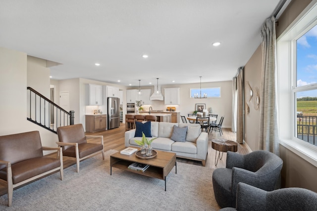 living room with light wood finished floors, healthy amount of natural light, recessed lighting, stairs, and a chandelier